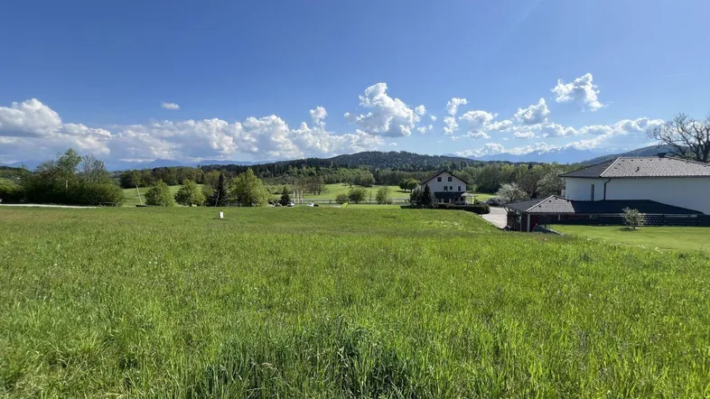 Weitläufige grüne Wiese mit Blick auf die umliegende Landschaft und Berge unter blauem Himmel.