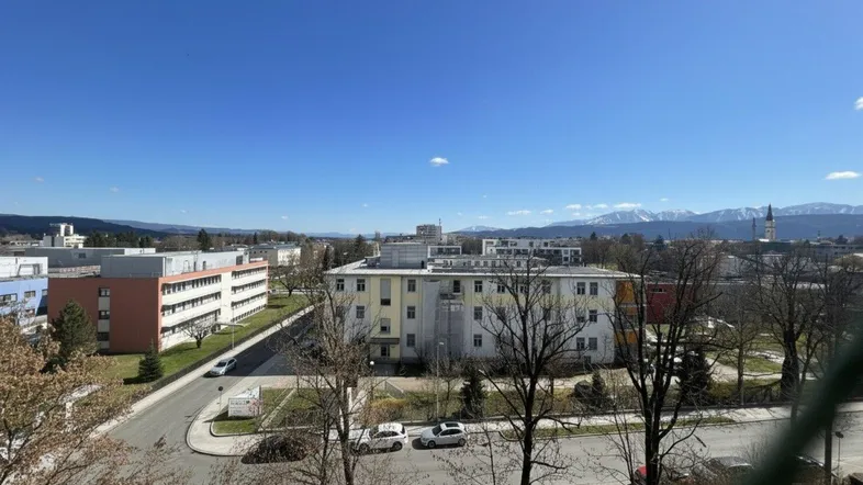 Weitblick über die Stadt mit Bergen im Hintergrund unter blauem Himmel.