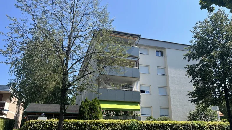 Mehrfamilienhaus mit mehreren Balkonen und grüner Markise an einem sonnigen Tag.