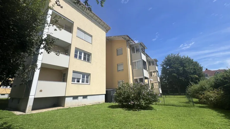 Mehrfamilienhaus mit gelber Fassade und Grünflächen in sonniger Umgebung.