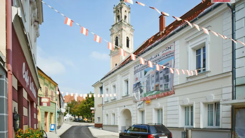 Blick auf eine belebte Straße in einer historischen Stadt mit traditionellen Gebäuden und einem Kirchturm im Hintergrund.
