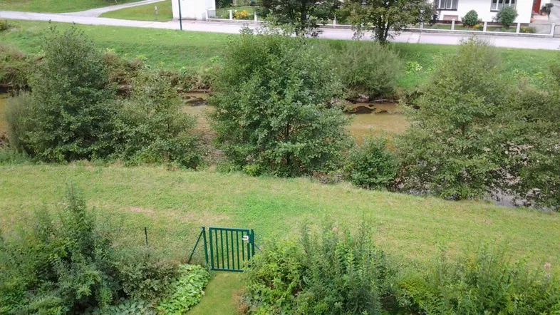 Weitläufiger Blick auf grüne Wiesen, einen kleinen Fluss und die umliegende Naturlandschaft.