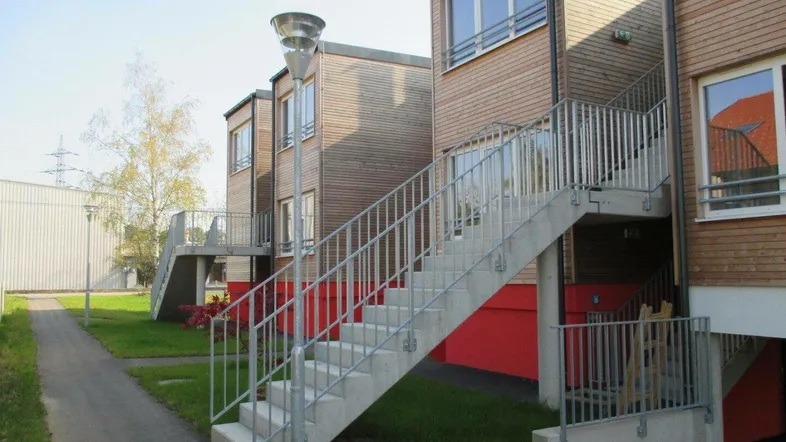 Moderne Reihenhäuser mit Holzfassade und Außentreppen in einer grünen Umgebung.