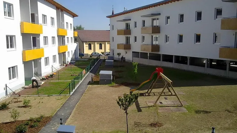 Moderne Wohngebäude mit gelben Balkonen, einem Spielplatz und gepflegten Grünflächen im Innenhof.