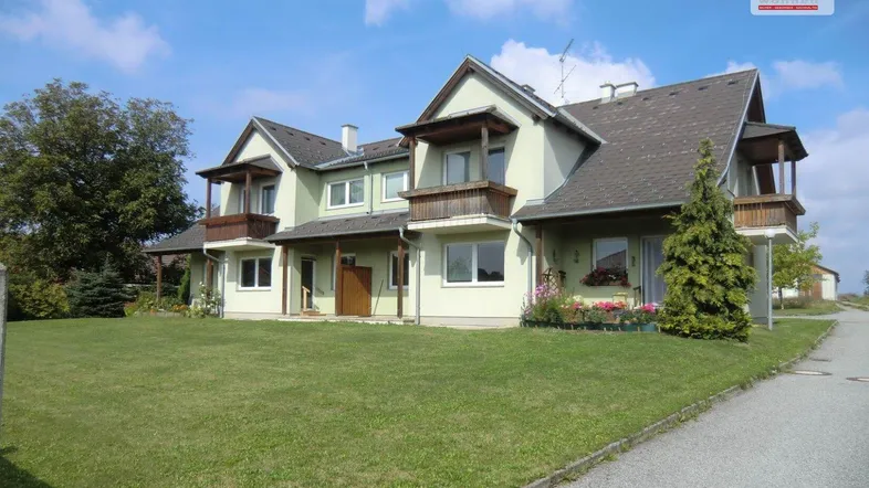 Mehrfamilienhaus mit mehreren Balkonen und gepflegtem Vorgarten unter blauem Himmel.