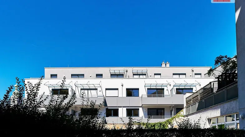 Moderne Wohnanlage mit weißer Fassade und blauen Akzenten unter klarem Himmel.