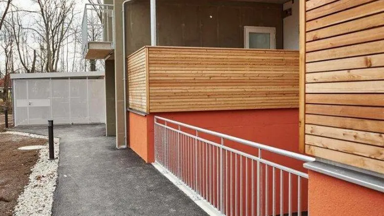 Moderner Eingangsbereich eines Neubaus mit barrierefreier Rampe und Holzverkleidung an den Balkonen.