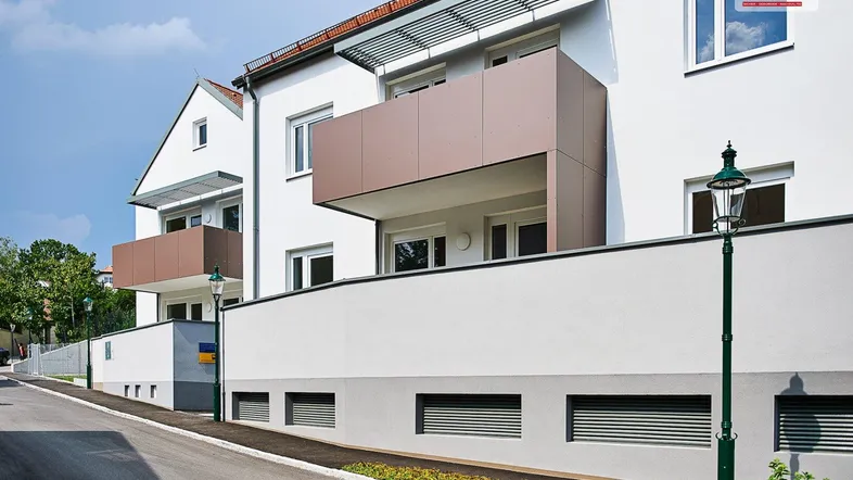 Moderne Wohnanlage mit weißer Fassade und braunen Balkonen unter blauem Himmel.