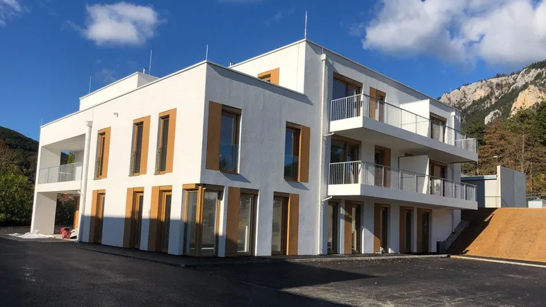Modernes Mehrfamilienhaus mit Balkonen und Holzfenstern vor einer malerischen Bergkulisse.
