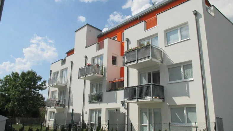 Modernes Mehrfamilienhaus mit weißer Fassade, orangefarbenen Akzenten und mehreren Balkonen.
