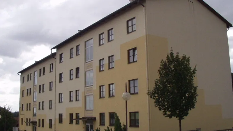Mehrfamilienhaus mit beiger und gelber Fassade unter bewölktem Himmel und einem Baum davor.