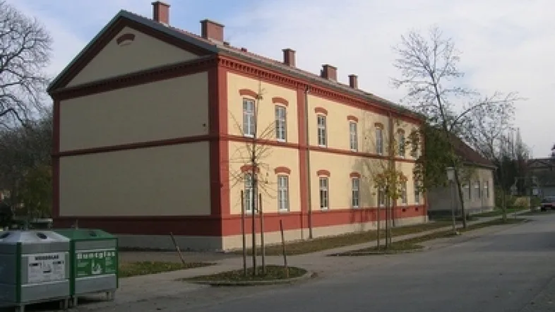 Gut erhaltenes Altbaugebäude mit beiger Fassade und roten Akzenten an einem sonnigen Tag.