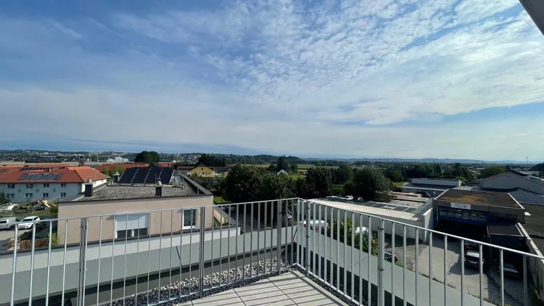 Weitblick von einem Balkon oder einer Terrasse über die umliegende Landschaft und Dächer unter blauem Himmel.