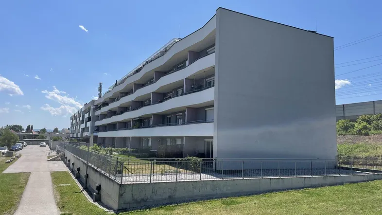 Moderne Wohnanlage mit mehreren Balkonen und gepflegten Grünflächen unter blauem Himmel.