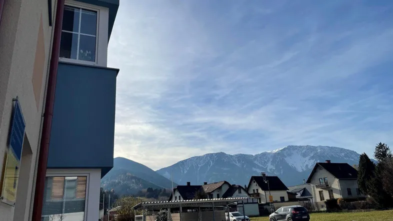 Moderne Wohnanlage mit blauer Fassade und Blick auf die umliegende Berglandschaft unter blauem Himmel.