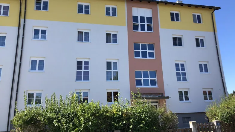 Mehrfamilienhaus mit farbiger Fassade, vielen Fenstern und gepflegter Hecke im Vordergrund.