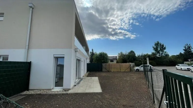 Moderne Neubaufassade mit angrenzender, noch ungestalteter Außenfläche unter bewölktem Himmel.