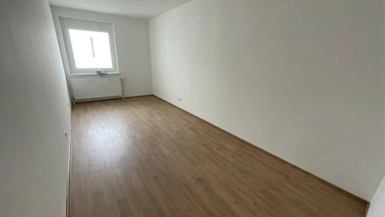 Helles Zimmer mit Holzfußboden und Fenster, ideal als Schlafzimmer oder Büro nutzbar.