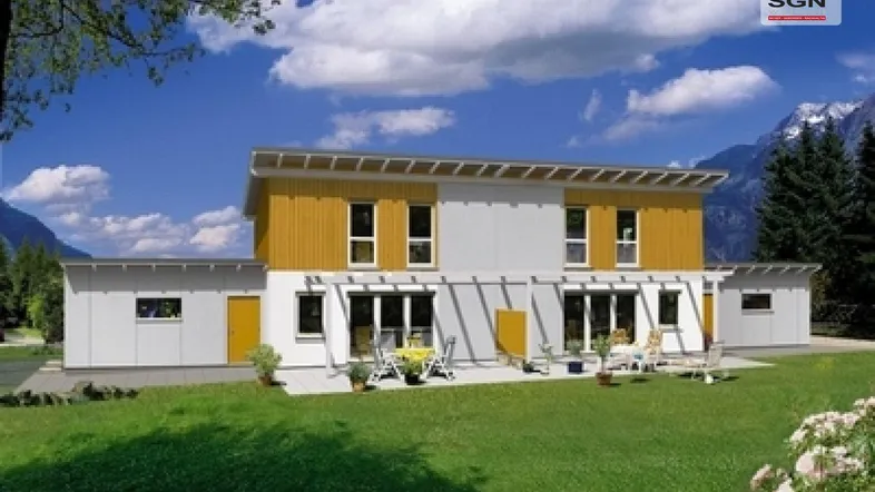 Modernes Einfamilienhaus mit gelber Fassade, Terrasse, Garten und Bergblick im Hintergrund.