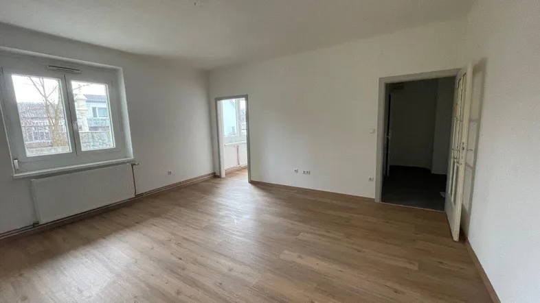 Helles, leeres Zimmer mit Laminatboden und Heizkörper unter dem Fenster, bereit zur Einrichtung.