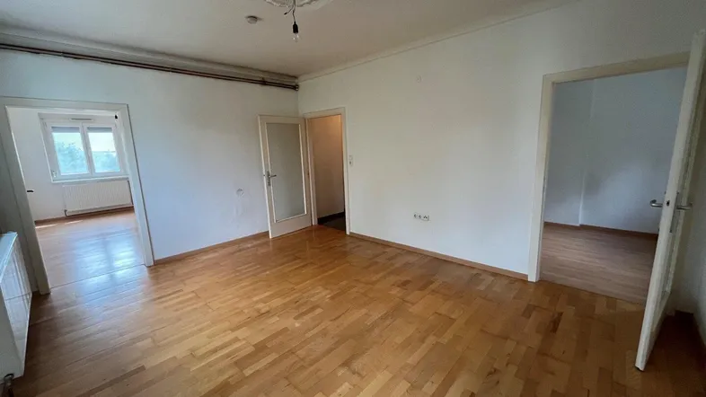 Helles, leeres Zimmer mit Parkettboden und Stuckdecke, bereit zur individuellen Gestaltung.