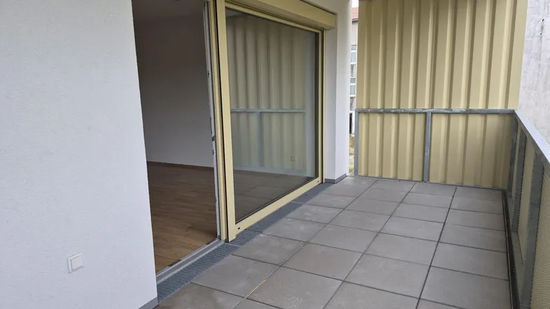 Geräumiger Balkon mit Fliesenboden und Schiebetür, die zu einem hellen Innenraum führt.