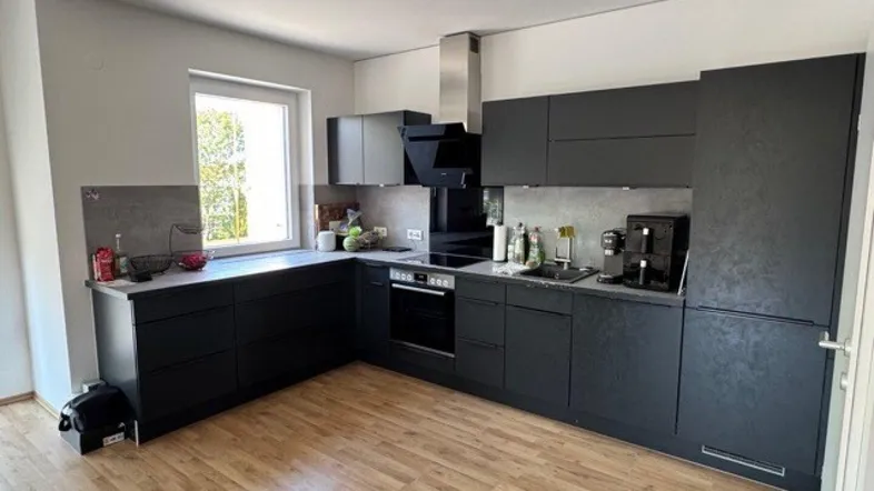 Moderne Küche mit dunklen Schränken, hellem Holzboden und Fenster mit Blick ins Grüne.