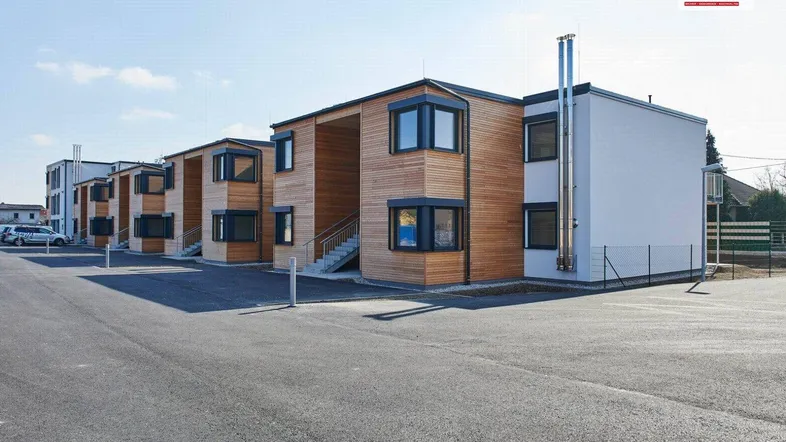 Moderne Wohnanlage mit Holzfassade, weißen Elementen und Parkplätzen unter blauem Himmel.