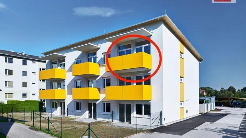 Modernes Mehrfamilienhaus mit weißer Fassade und leuchtend gelben Balkonen unter blauem Himmel.