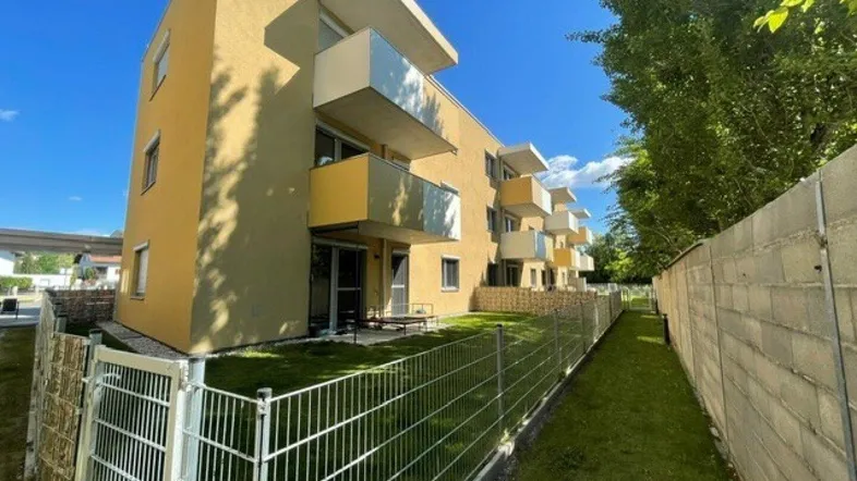 Ansicht eines modernen Wohngebäudes mit gelber Fassade, Balkonen und einem kleinen privaten Gartenbereich.