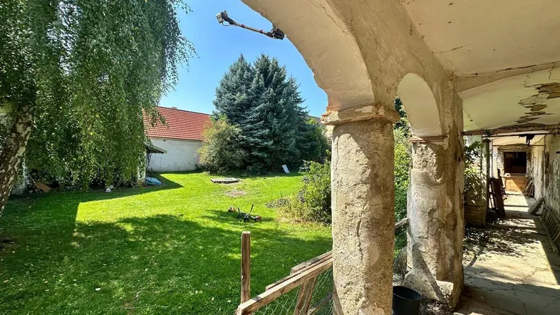 Alter, überdachter Gang mit Bögen und Blick auf den grünen Gartenbereich.