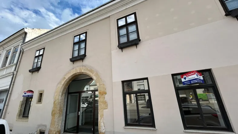 Historische Fassade eines Gebäudes mit großem Steinbogen-Eingang und modernen Fenstern zur Straße.