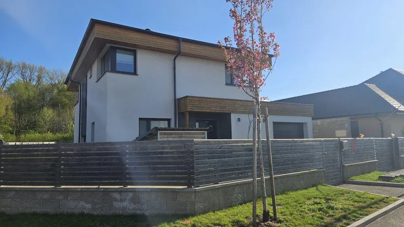 Modernes Einfamilienhaus mit weißer Fassade, Holzelementen und gepflegtem Vorgarten.