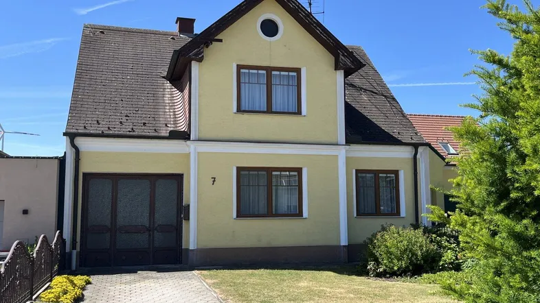 Vorderansicht eines traditionellen gelben Einfamilienhauses mit Satteldach und gepflasterter Einfahrt.