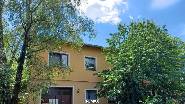 Gelbe Fassade eines Einfamilienhauses umgeben von üppigem Grün unter blauem Himmel.