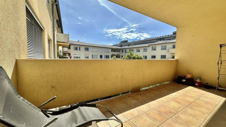 Balkon mit Fliesenboden und Blick auf die umliegenden Gebäude, ausgestattet mit einem Liegestuhl.