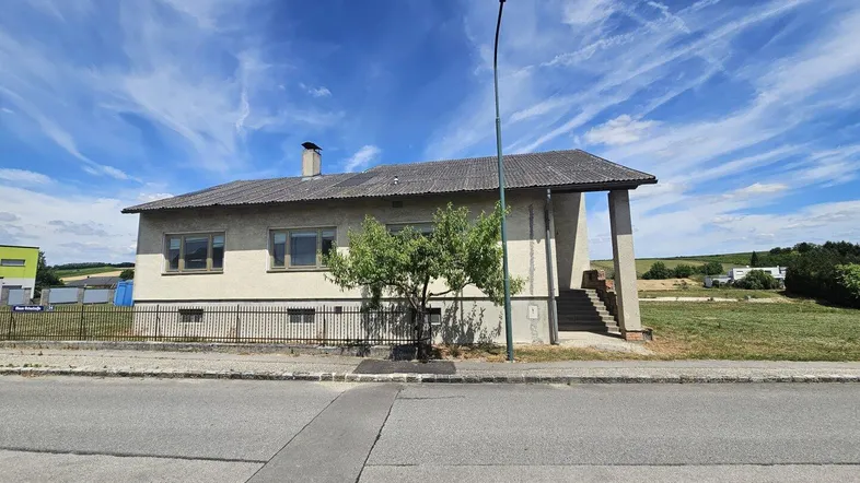 Einfaches Einfamilienhaus mit Satteldach und kleiner Grünfläche an der Straße.