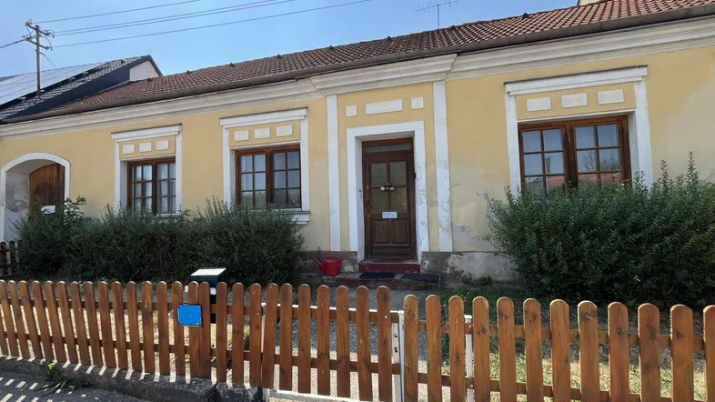 Gelbe Fassade eines traditionellen Hauses mit Holzzaun und grünen Büschen im Vorgarten.