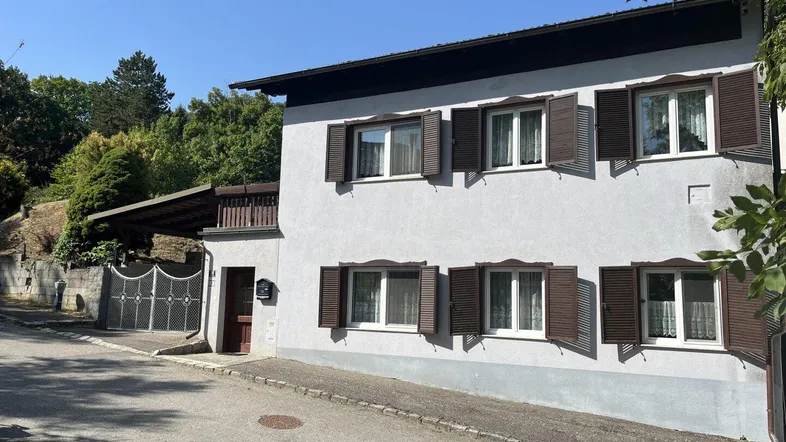 Vorderansicht des Hauses mit braunen Fensterläden, Carport und gepflegter Zufahrt.