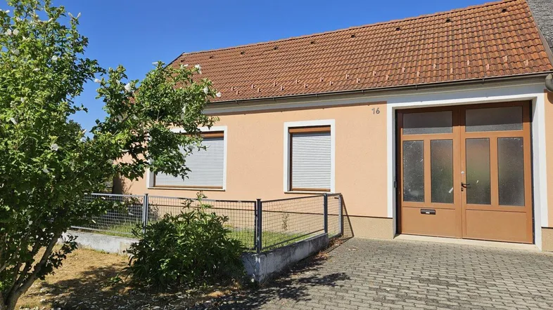 Vorderansicht eines Einfamilienhauses mit gepflasterter Einfahrt und kleinen Bäumen unter blauem Himmel.