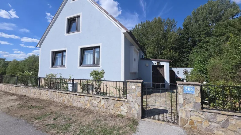 Helles Einfamilienhaus mit hellblauer Fassade, Satteldach und Steinmauer am Eingangsbereich.