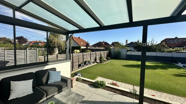 Überdachte Terrasse mit bequemen Gartenmöbeln und Blick auf den gepflegten Rasen und die Nachbarschaft.
