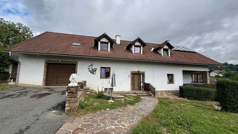 Traditionelles Einfamilienhaus mit Satteldach, Gauben und Solarpaneelen in ländlicher Umgebung.