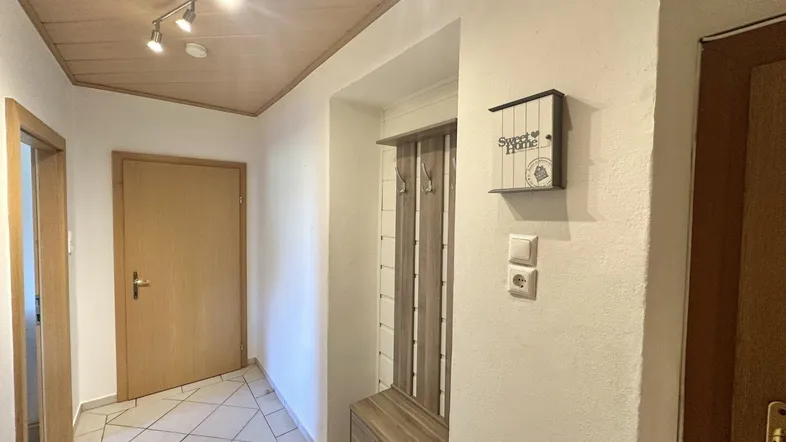 Heller Eingangsbereich mit Fliesenboden, Holzdecke und praktischer Garderobenlösung.