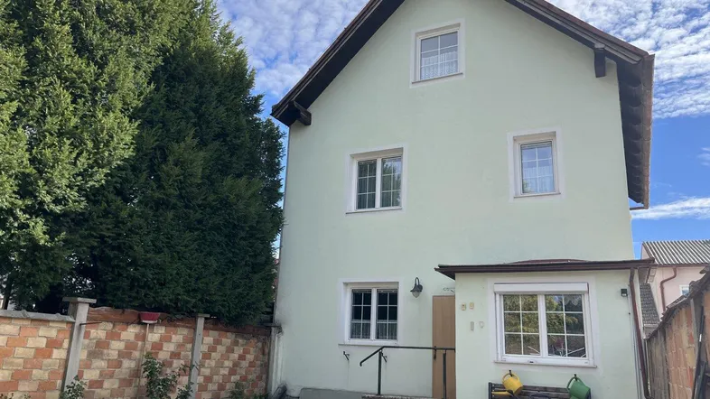 Helles Einfamilienhaus mit Satteldach und gepflegtem Gartenbereich unter blauem Himmel.