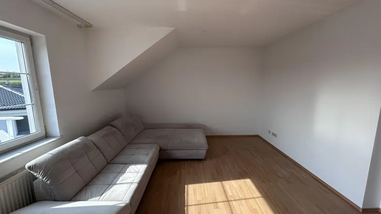Helles Wohnzimmer mit gemütlichem Ecksofa, Holzfußboden und Dachschräge, bietet einen Blick ins Grüne.
