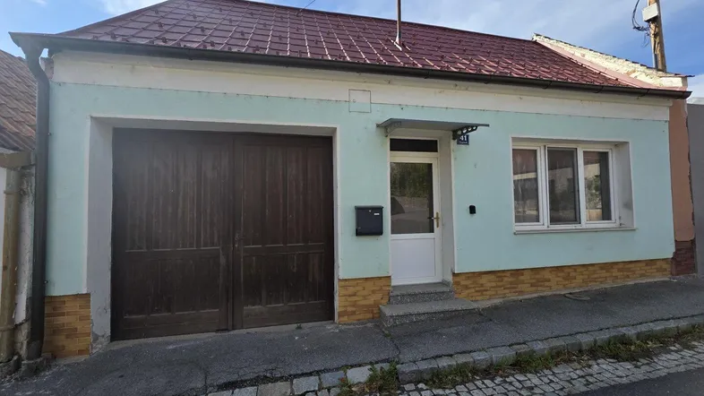 Hausfassade mit Garagentor und Eingangstür unter einem roten Ziegeldach.