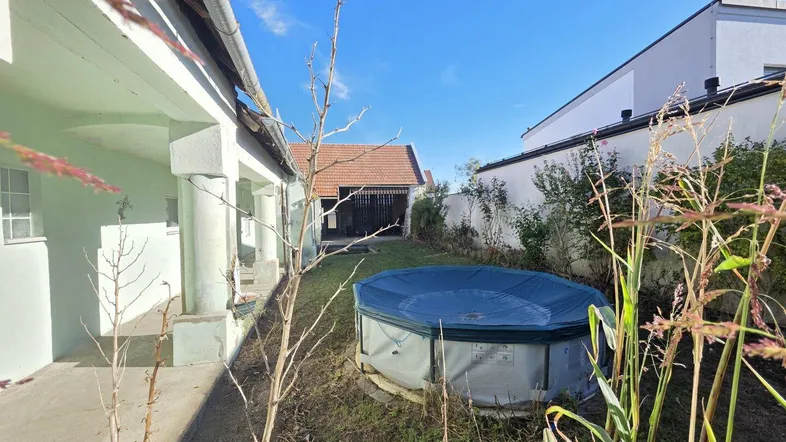 Hinterhof mit einem aufgestellten Pool und Blick auf das Nebengebäude unter blauem Himmel.