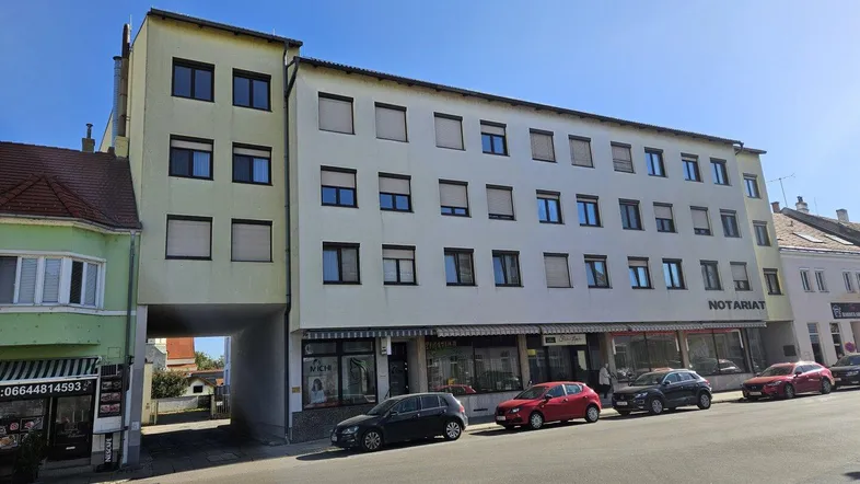 Mehrstöckiges Gebäude mit Geschäften im Erdgeschoss und Wohnungen darüber an einer Straße.