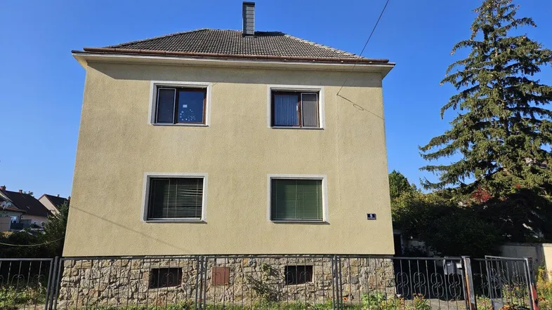 Gelbes Einfamilienhaus mit Satteldach und Steinsockel unter blauem Himmel.